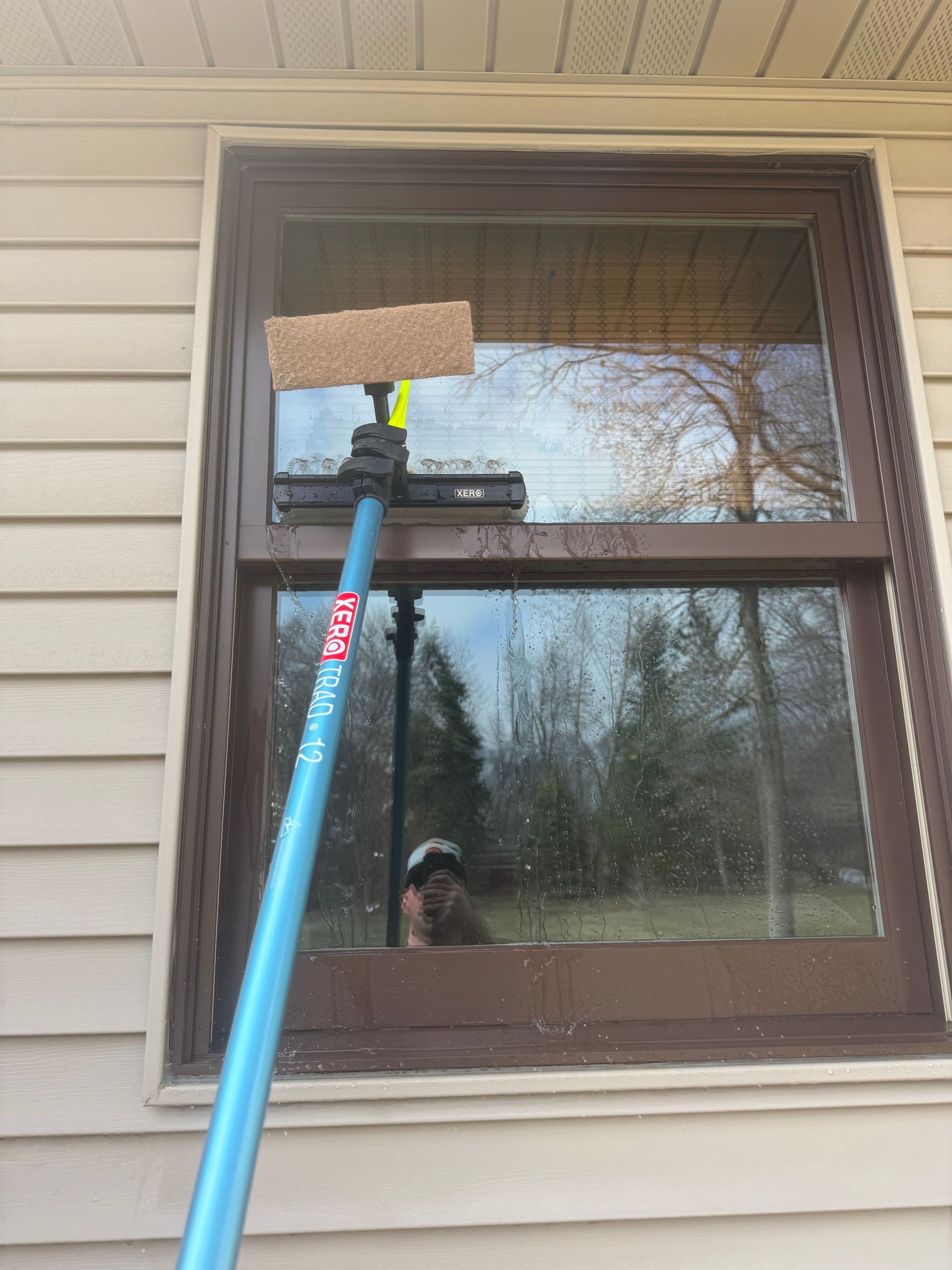 A person is cleaning a window with a sponge on a pole.