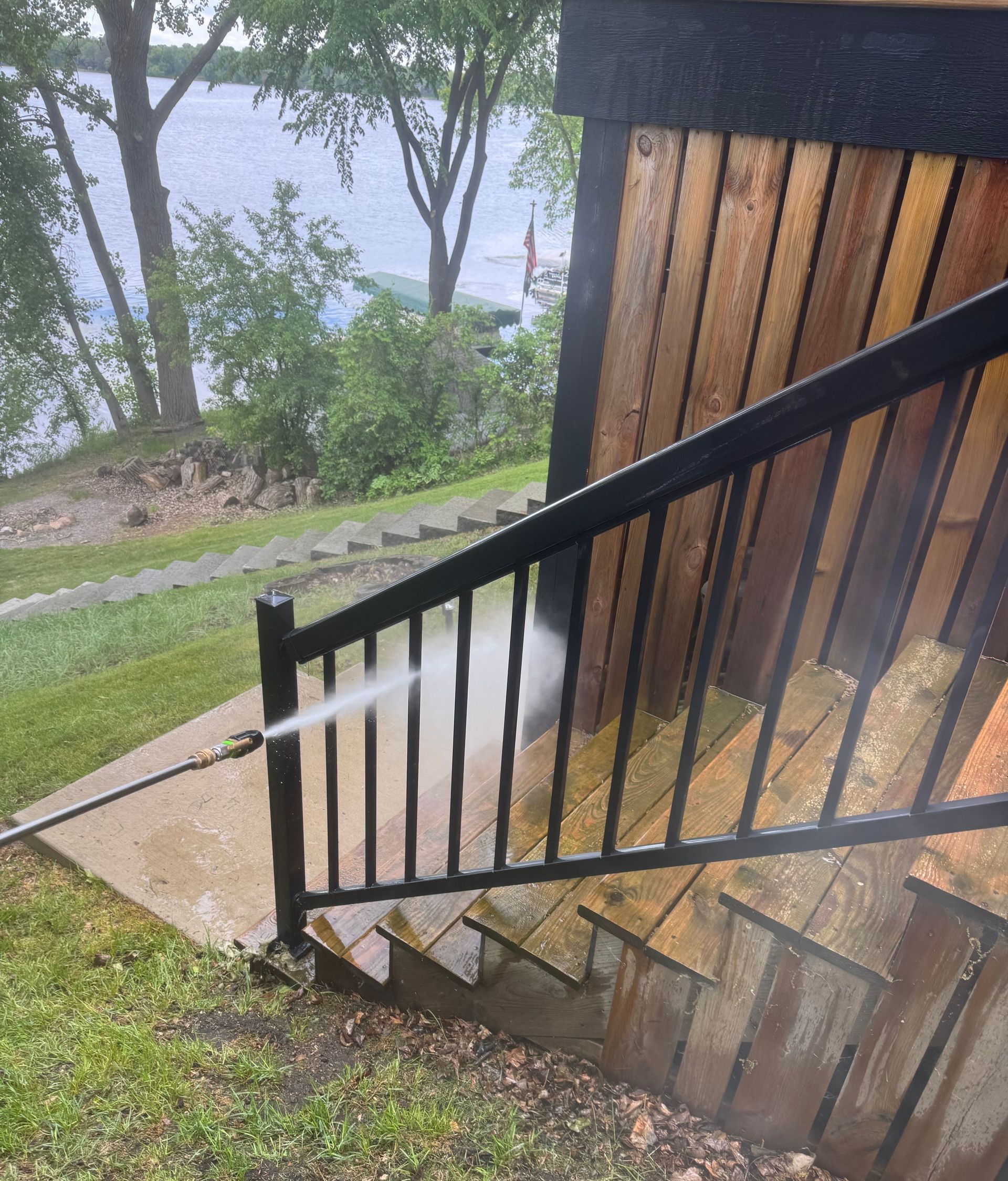 A person is cleaning a wooden railing with a high pressure washer.