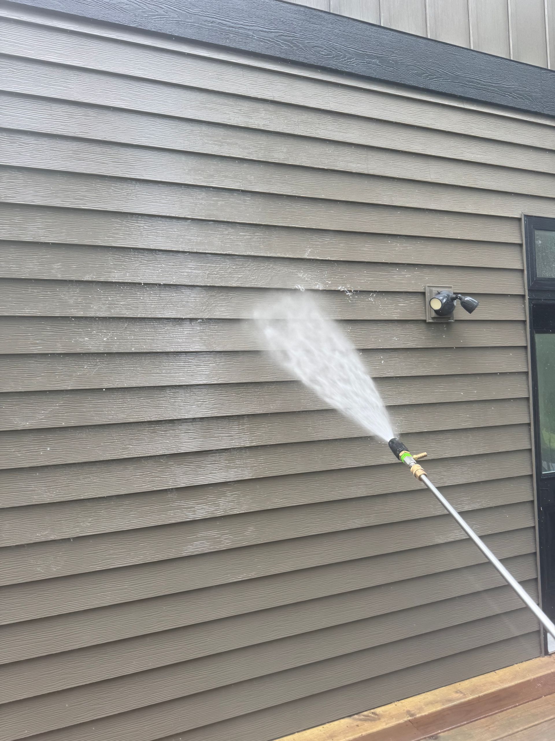 A person is using a pressure washer to clean the side of a house.