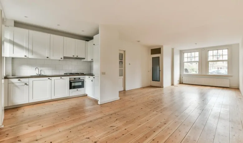 An empty kitchen with white cabinets and wooden floors.
