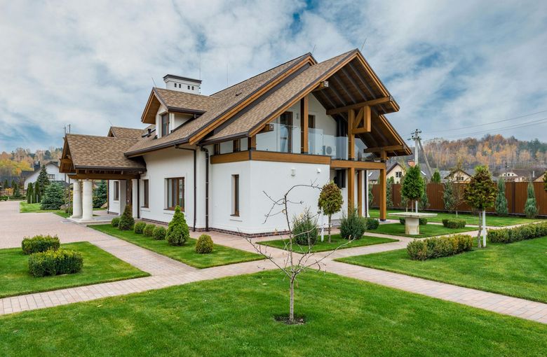 A large white house with a wooden roof and a lush green lawn in front of it.