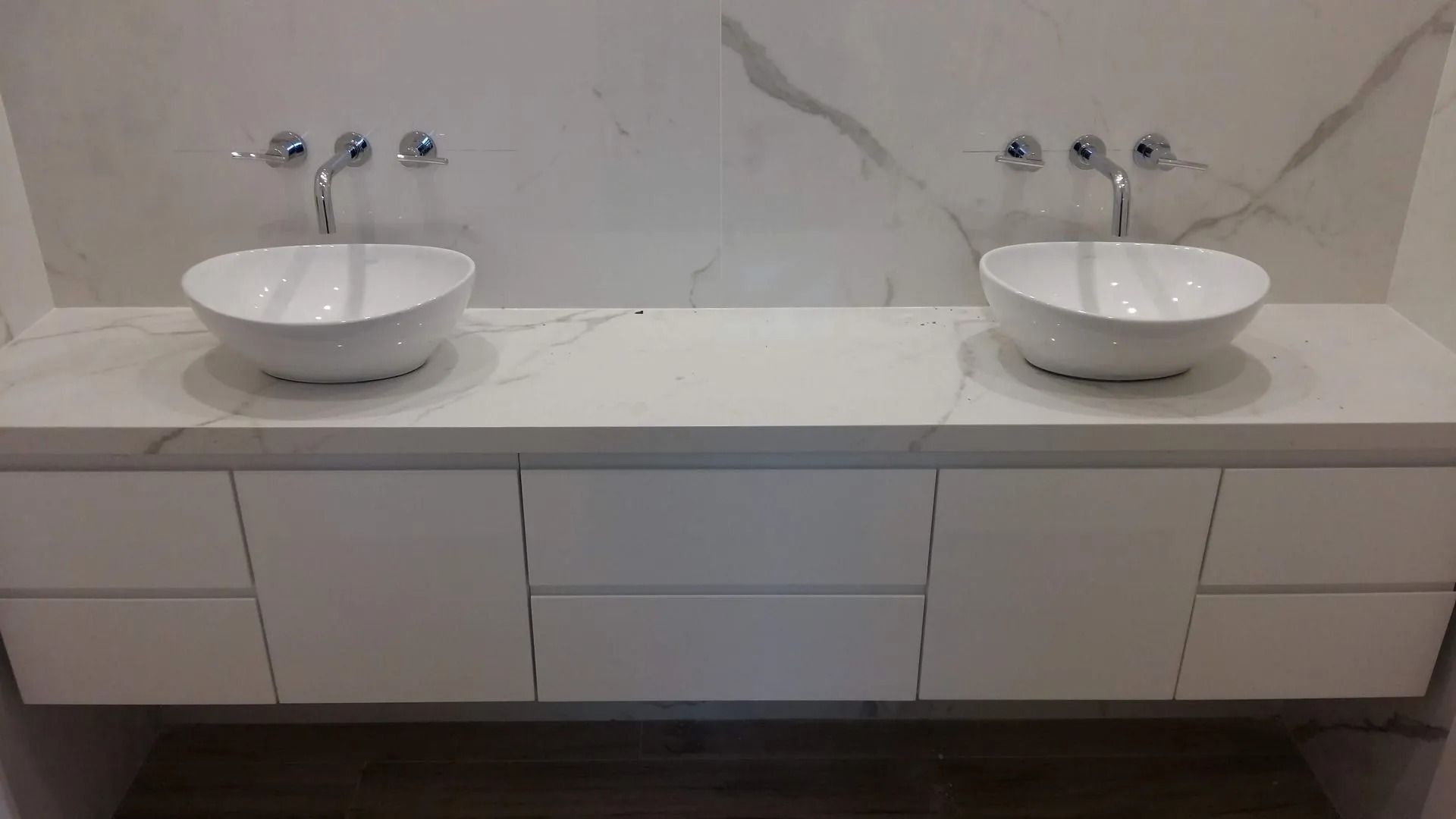 Tocador doble moderno con dos lavabos blancos sobre encimera y cajones en un baño minimalista.