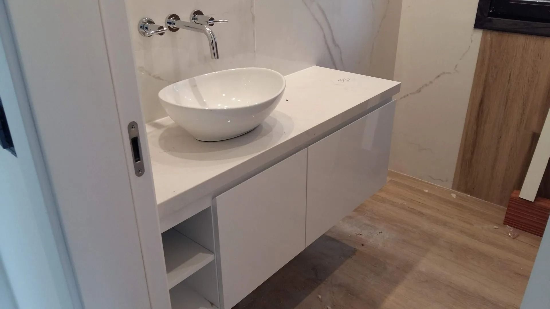 Tocador de baño moderno con lavabo blanco sobre encimera, armario con espejo y suelo de madera.