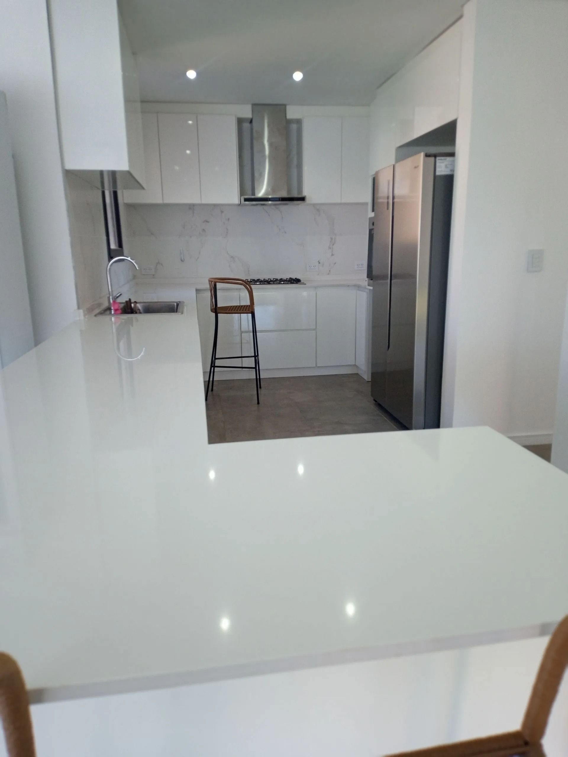 Cocina moderna blanca con electrodomésticos de acero inoxidable y una pequeña silla de comedor.