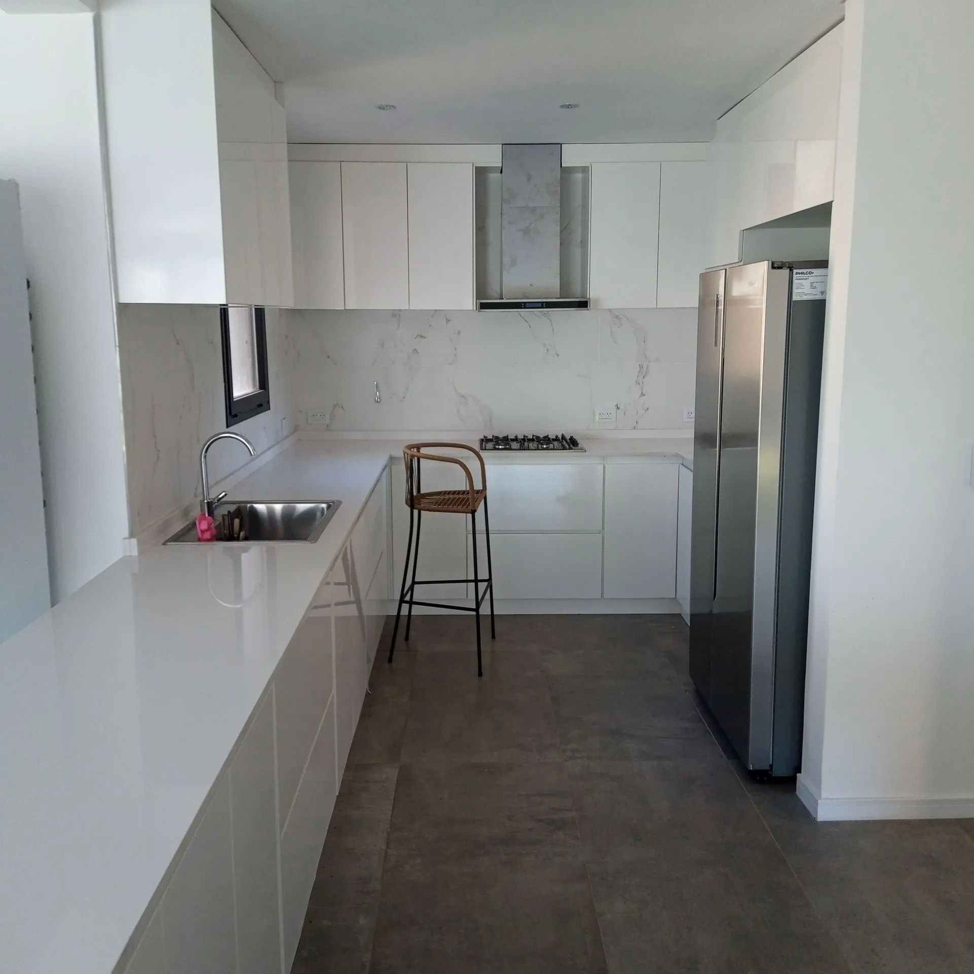 Cocina moderna blanca tipo galera con refrigerador de acero inoxidable, estufa y una silla en la encimera.