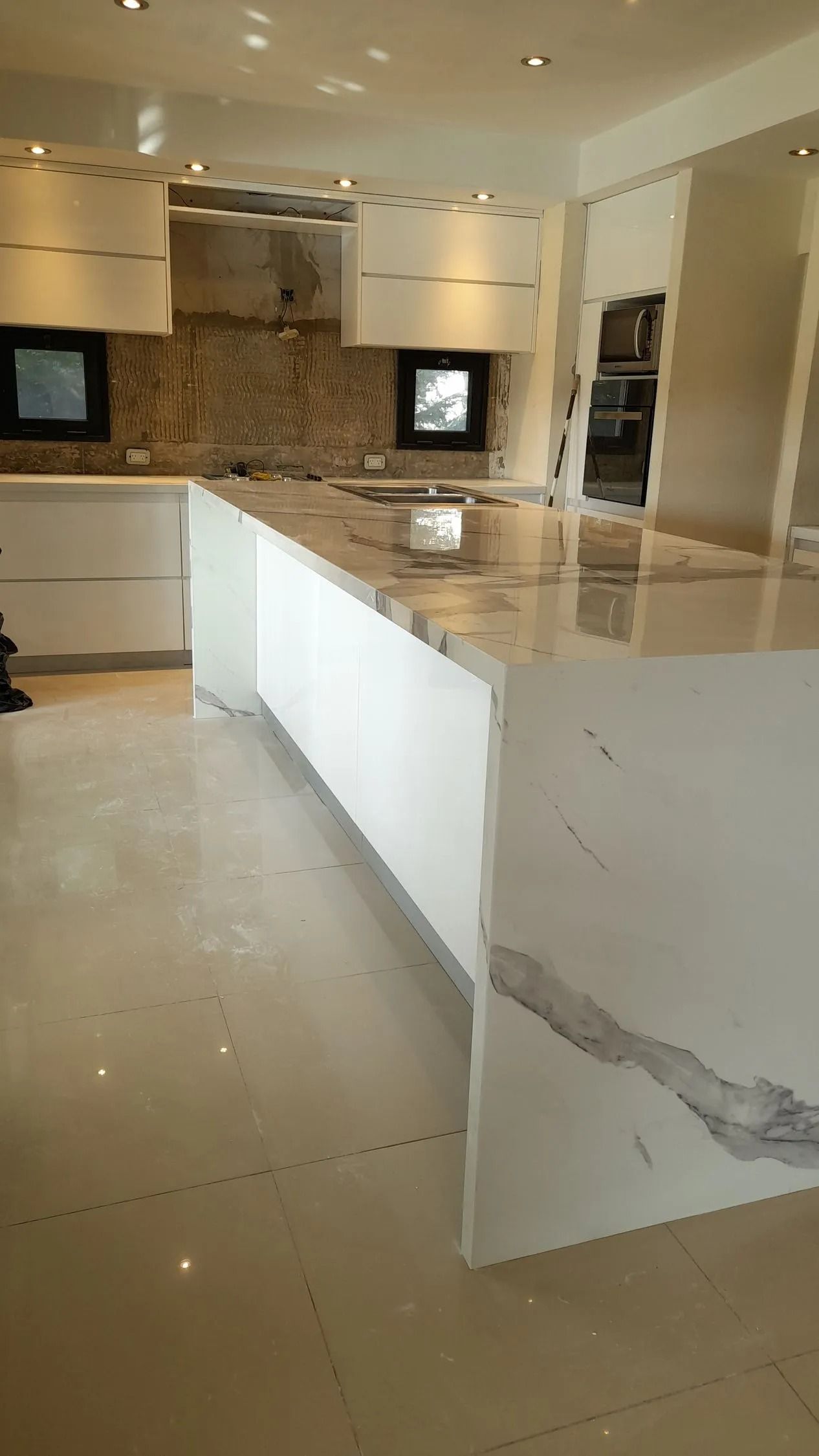 Cocina moderna con una gran isla blanca y encimeras de mármol brillante bajo iluminación empotrada.