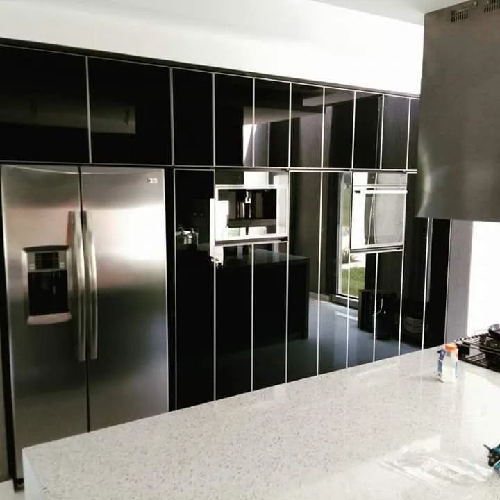 Cocina moderna con gabinetes negros brillantes, refrigerador de acero inoxidable y encimera de isla de piedra clara.