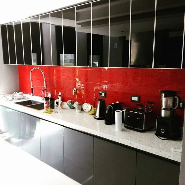 Encimera de cocina moderna con protector contra salpicaduras rojo, gabinetes negros y pequeños electrodomésticos.