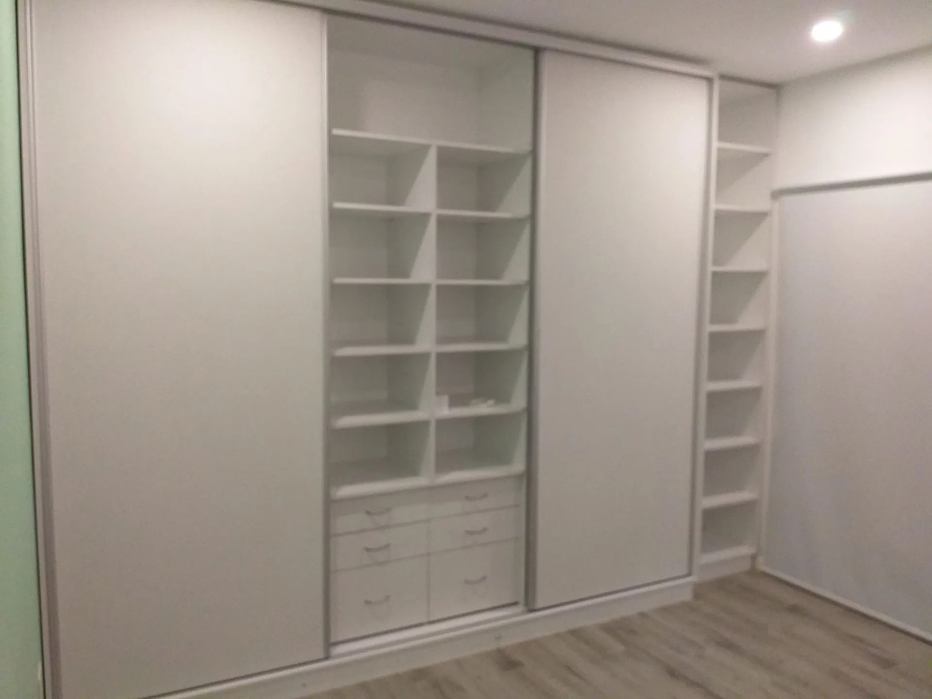 Armario empotrado blanco con estantes, cajones y puertas correderas en una habitación moderna y vacía.