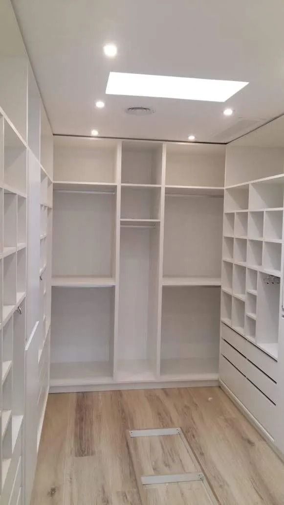 Vestidor vacío con estantes y cajones blancos empotrados, y una claraboya sobre suelo de madera.