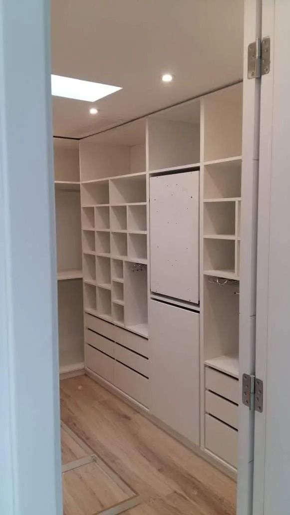 Armario empotrado blanco con estantes y cajones en un luminoso pasillo con suelo de madera.
