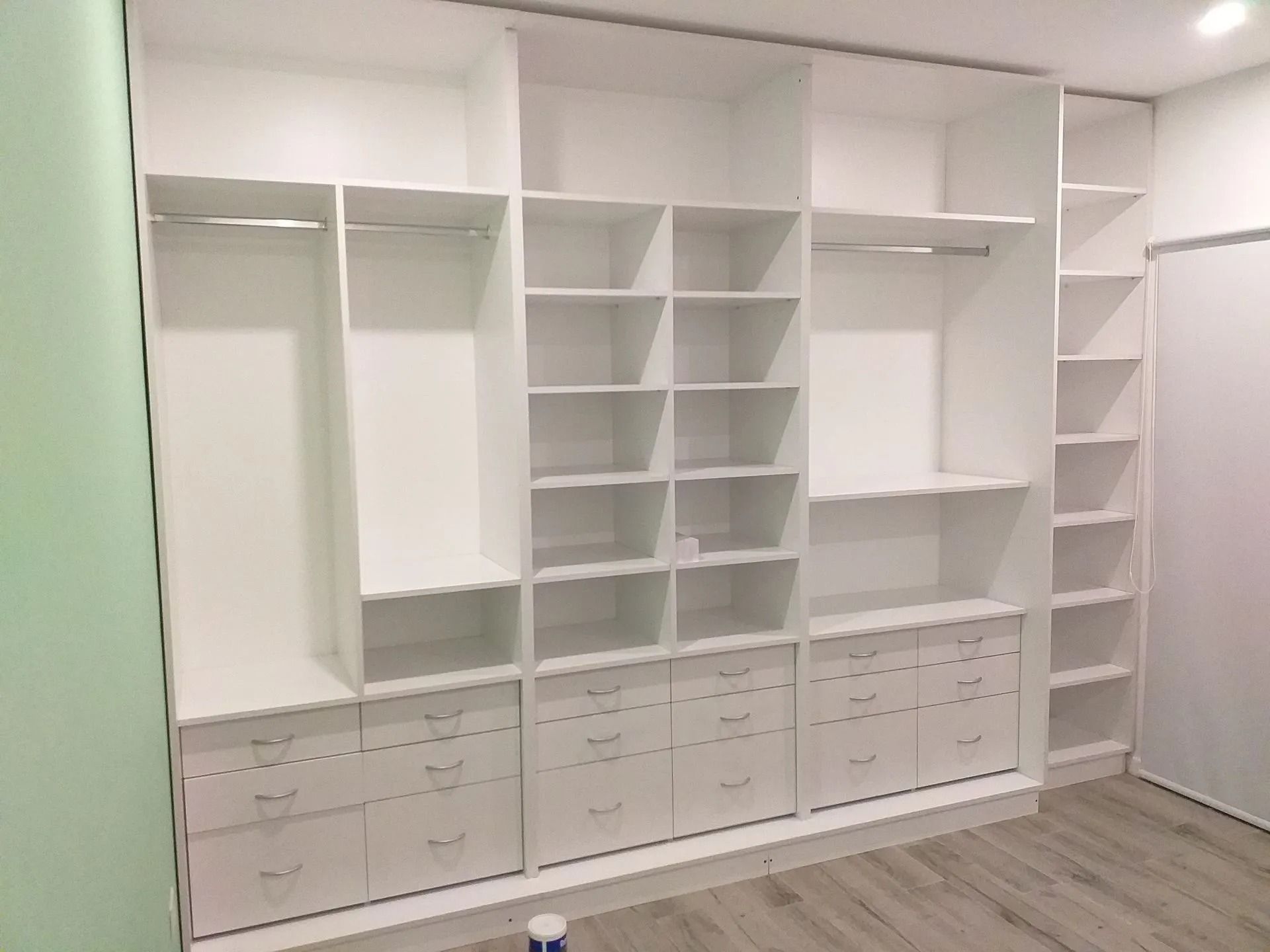 Organizador de armario blanco empotrado con estantes, barras para colgar ropa y cajones en una habitación vacía.