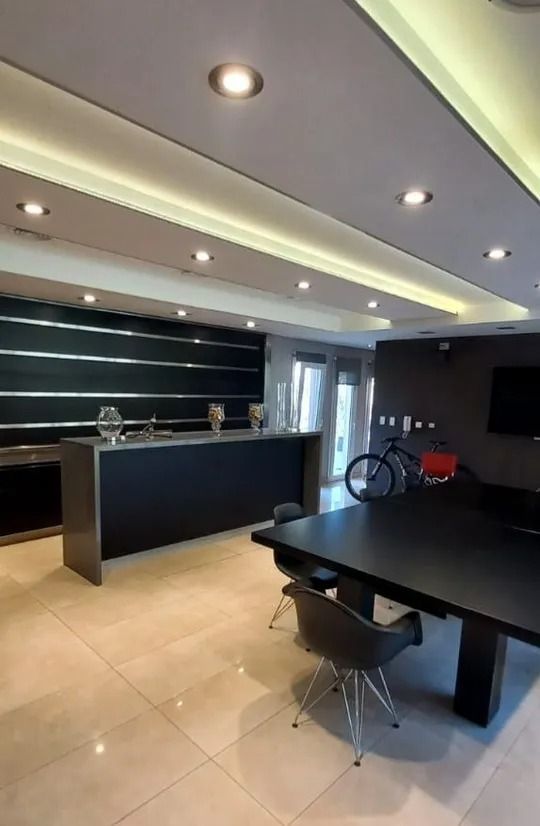 Cocina moderna con isla negra, suelo de baldosas beige, luces empotradas y una mesa de comedor en primer plano.