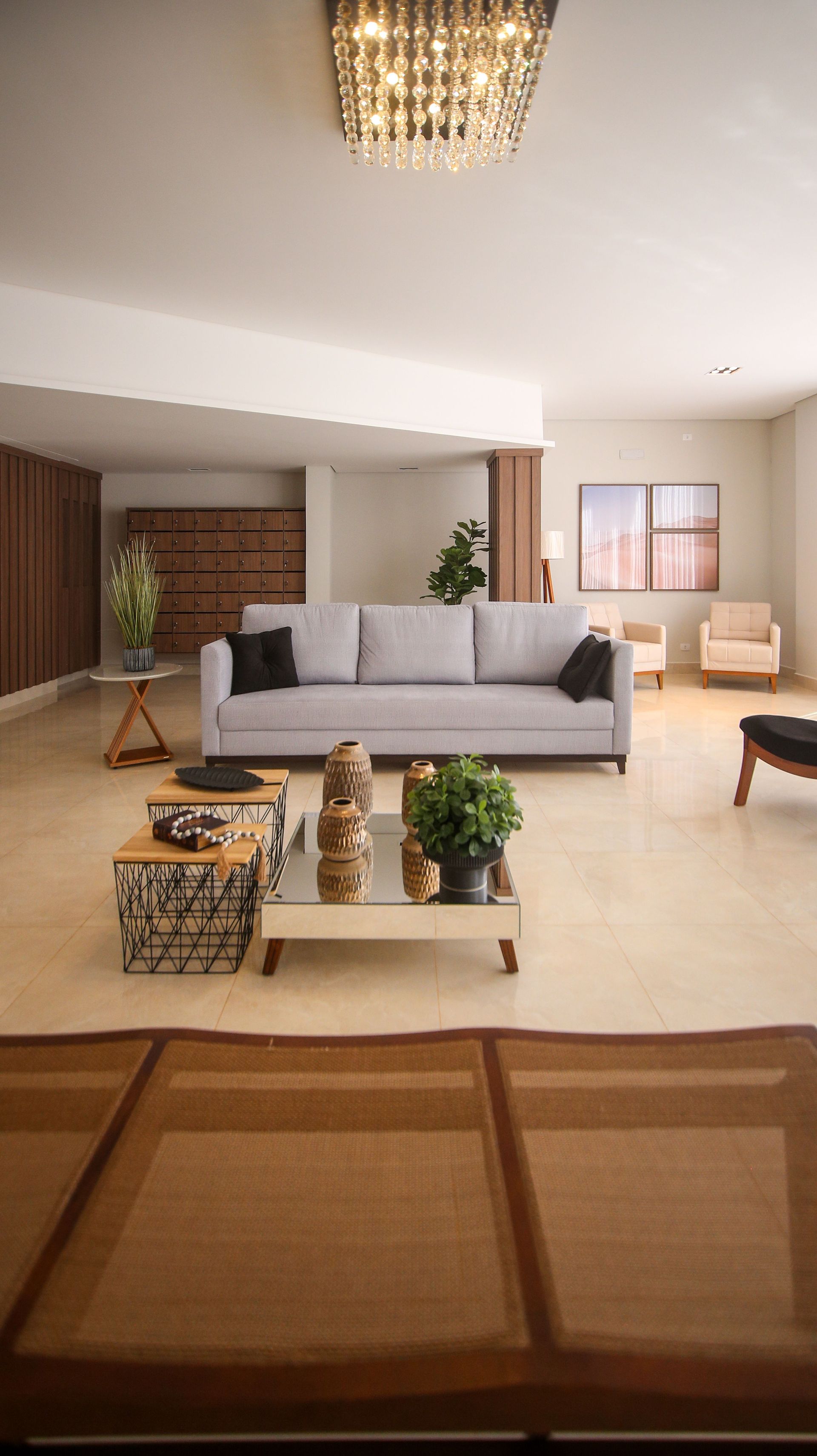 Sala de estar moderna con sofá gris, sillas beige, mesa de centro y lámpara de araña bajo iluminación cálida.