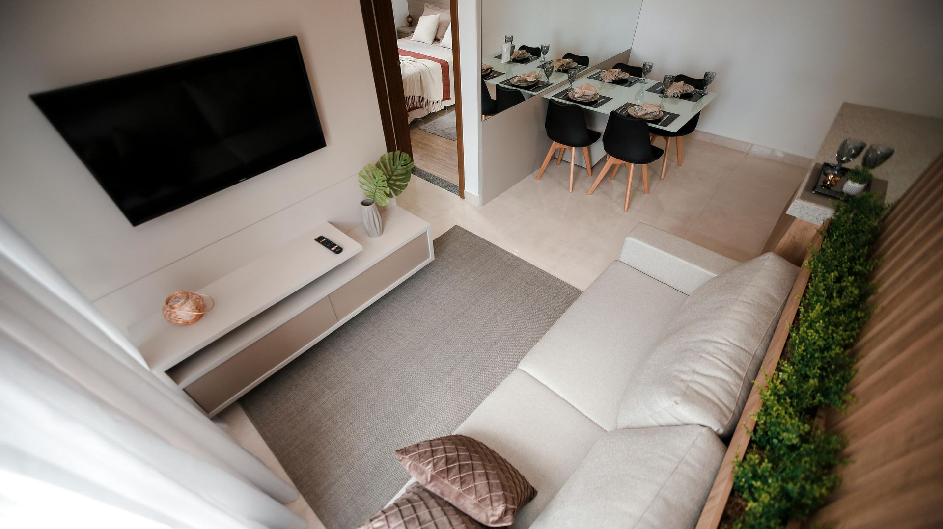 Luminoso salón moderno con sofá, televisor montado en la pared y zona de comedor en un espacio diáfano.
