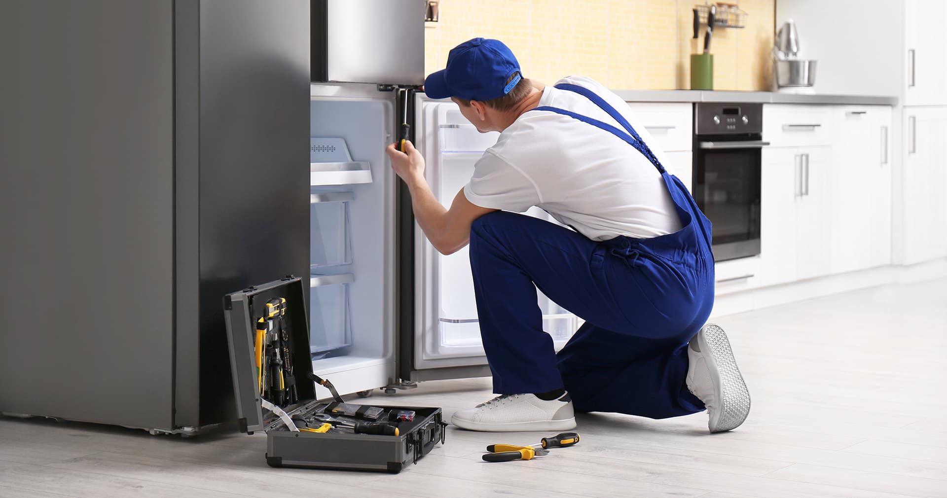 A man is repairing a refrigerator in a kitchen.