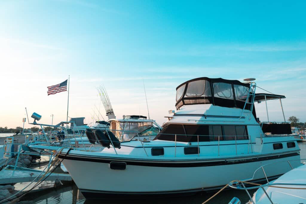 White motorboat with American flag docked in a harbor at sunset; blue sky.