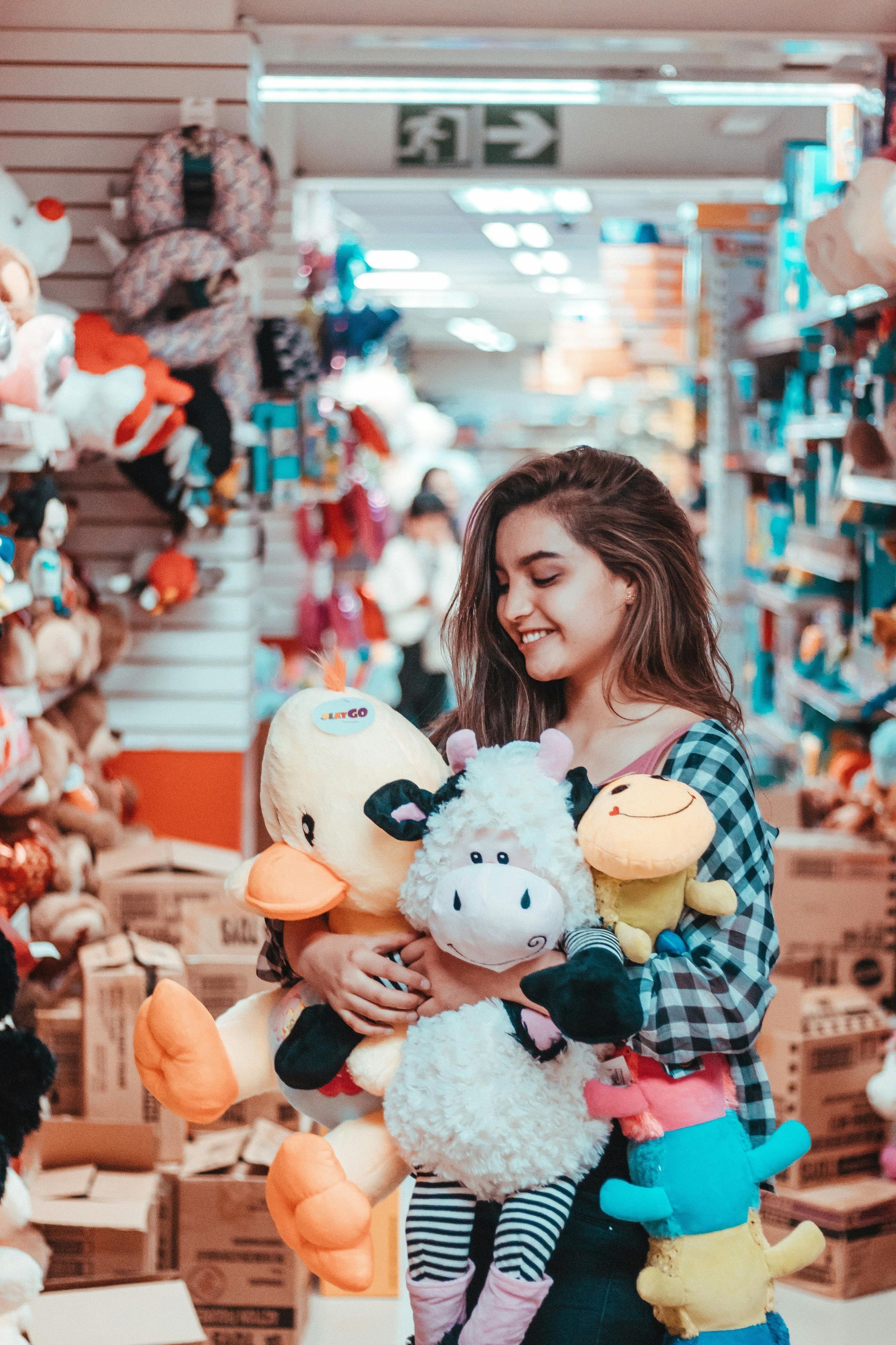 Woman smiling, holding several plush toys in a brightly lit toy store, surrounded by shelves of merchandise.