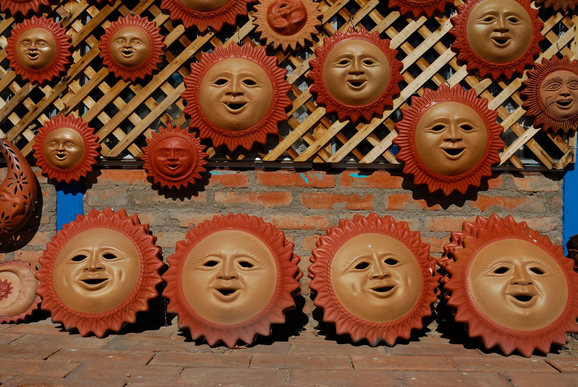 Terracotta sun faces with smiling expressions, displayed on a brick wall.