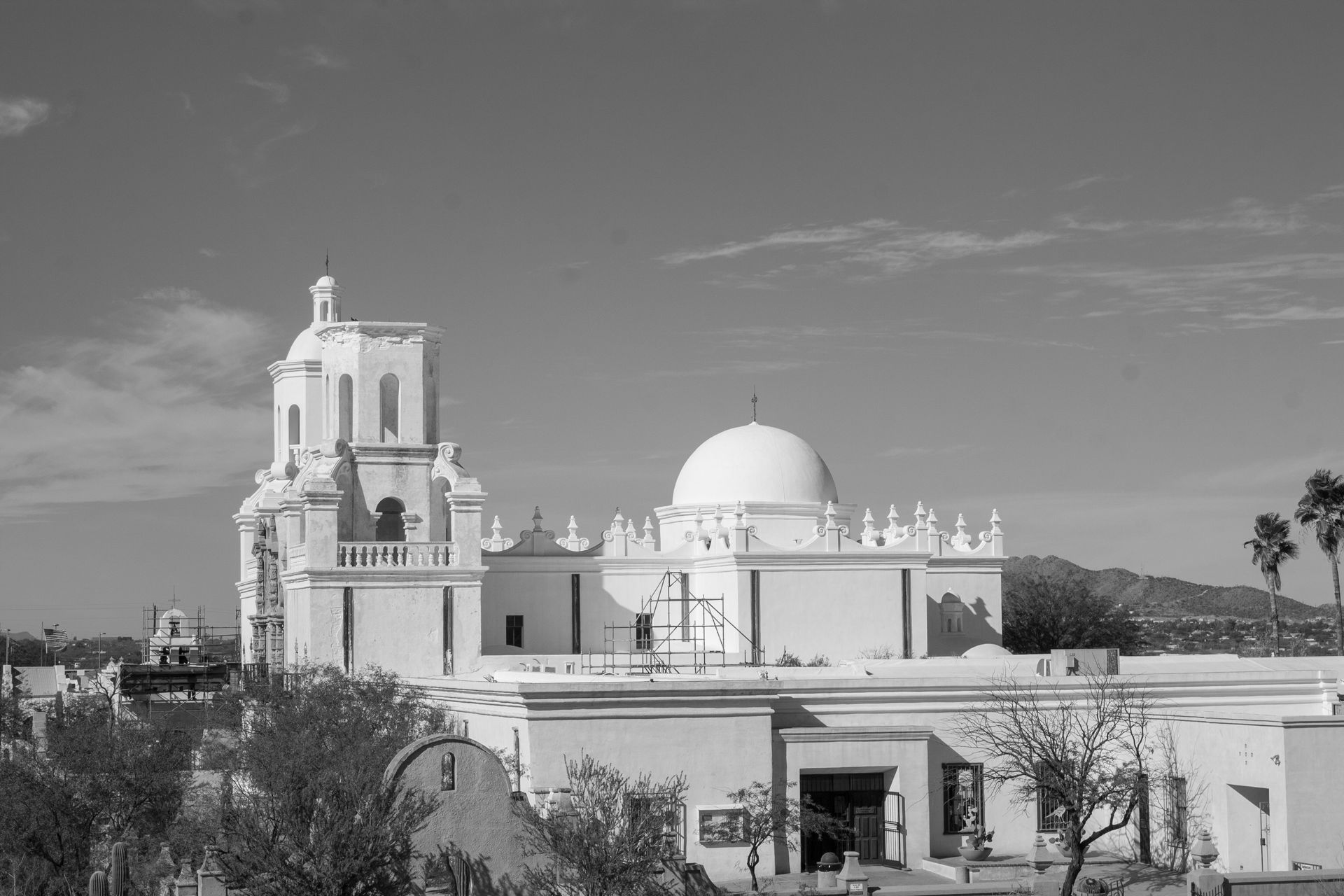 A white mission-style church with a domed roof and bell tower under a bright sky.