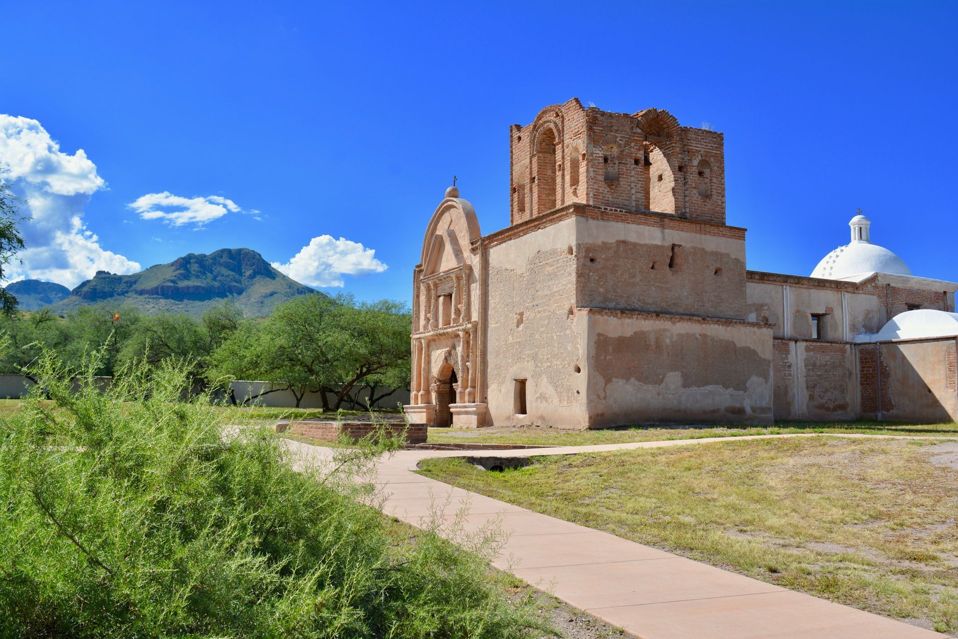 Historic San Xavier Mission, a tan adobe church with a broken tower, blue sky, and a mountain backdrop.