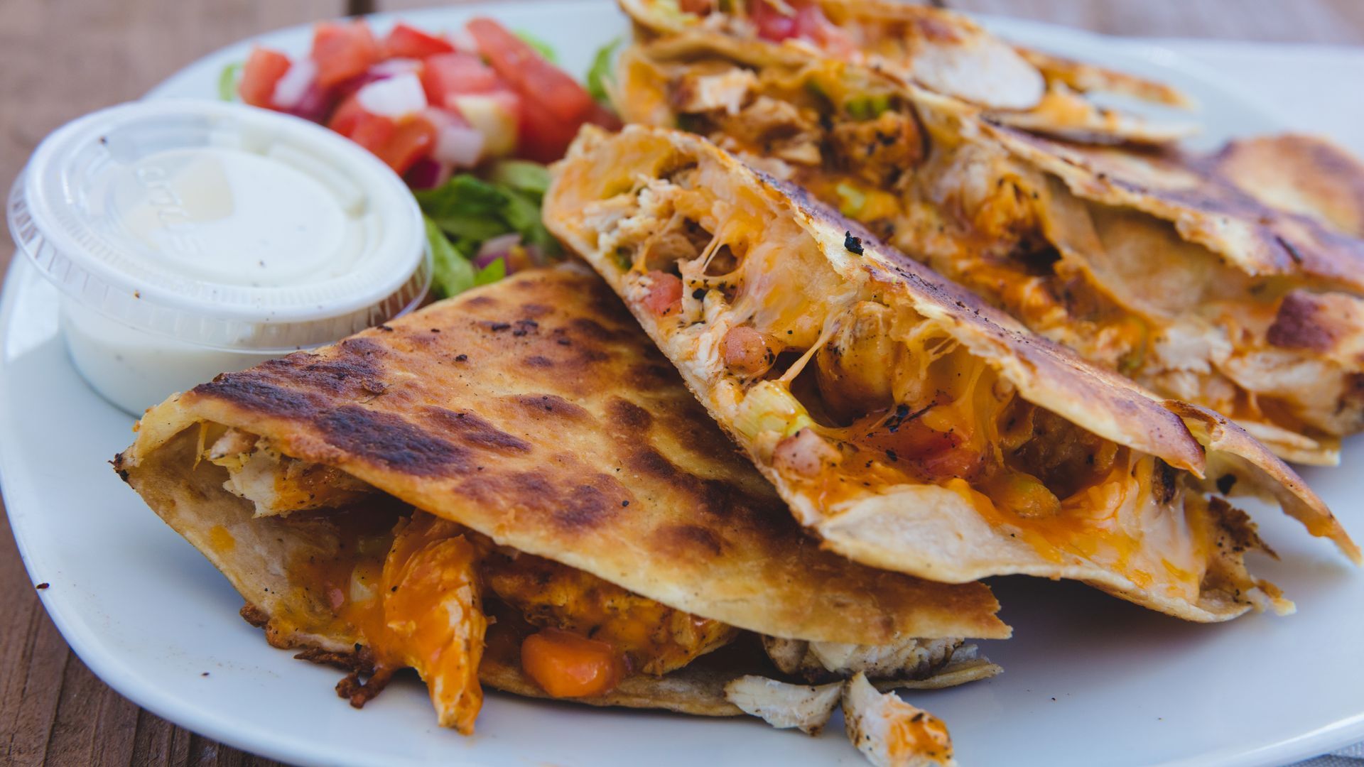 Plate of chicken quesadillas with melted cheese, served with dipping sauce and a side salad.