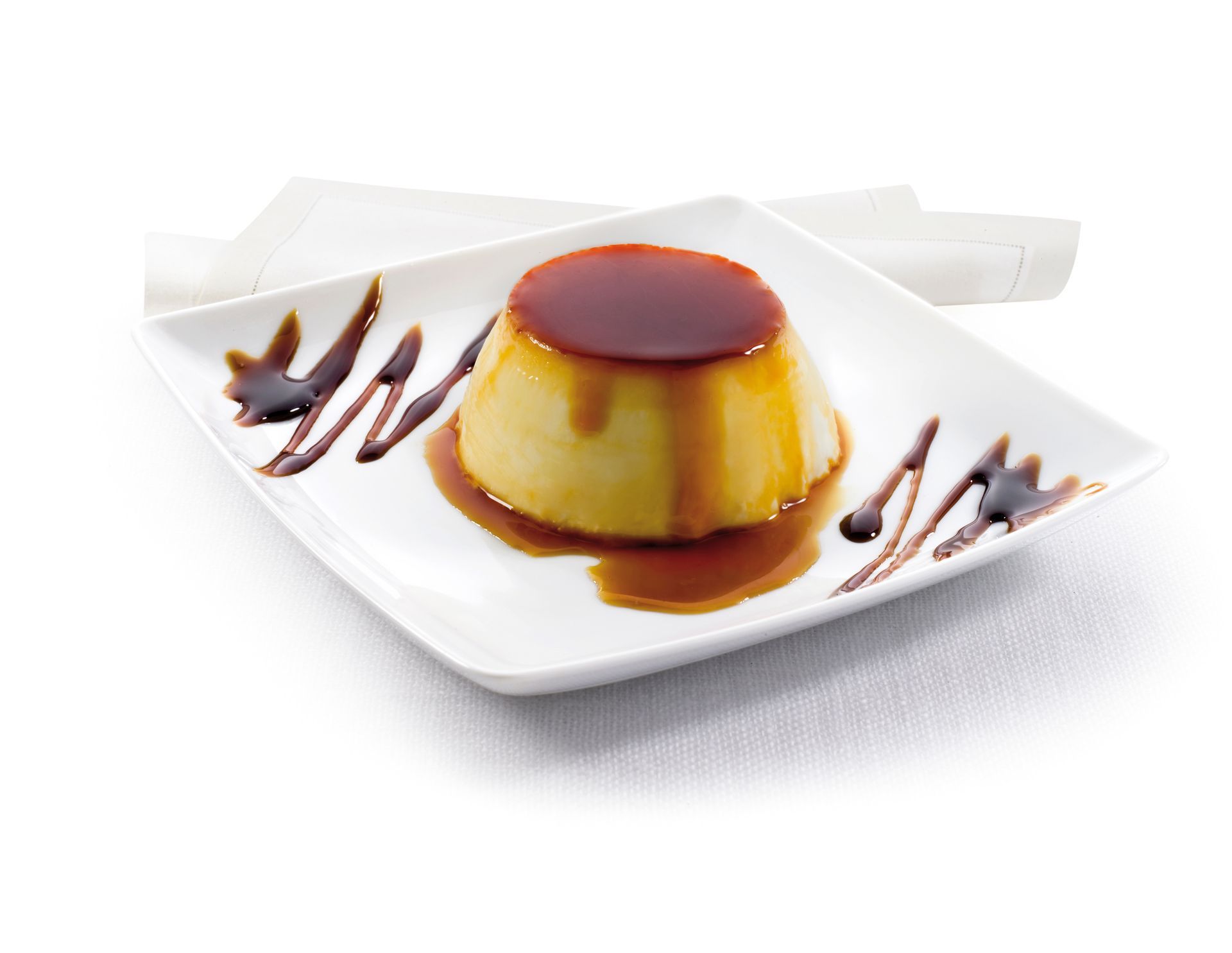 Flan with caramel sauce on a white square plate, garnished with drizzles, and a napkin in the background.