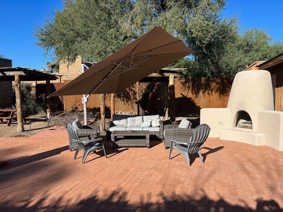 Outdoor patio with seating under a brown umbrella near a fireplace and a rustic wooden fence.