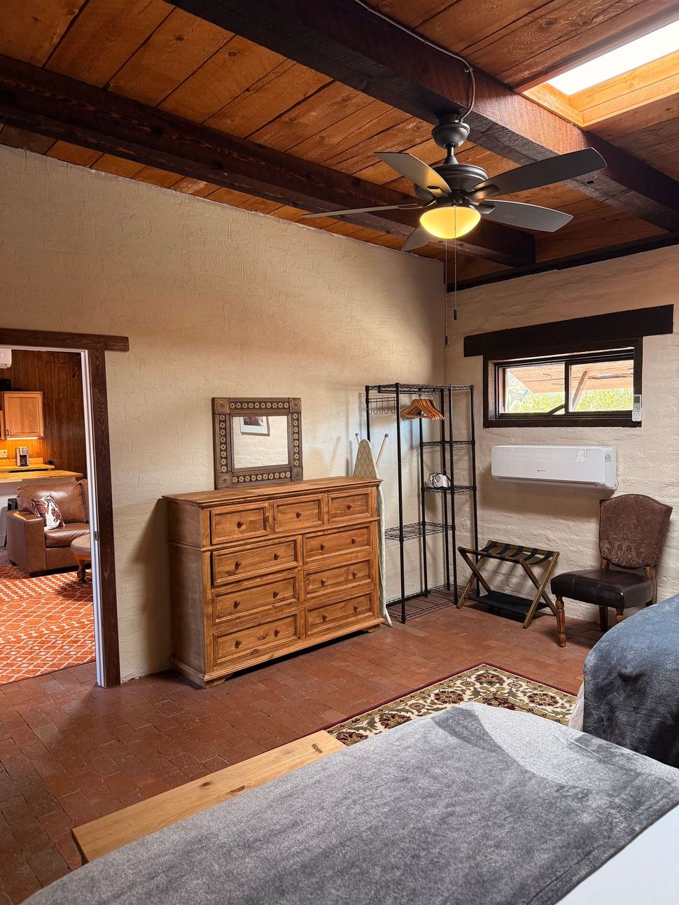 Bedroom with wooden ceiling beams, dresser, and bed; a doorway to another room.icon