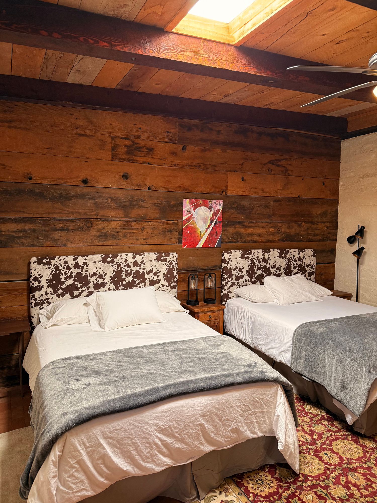 Two beds in a rustic room with wood paneling and a skylight.
