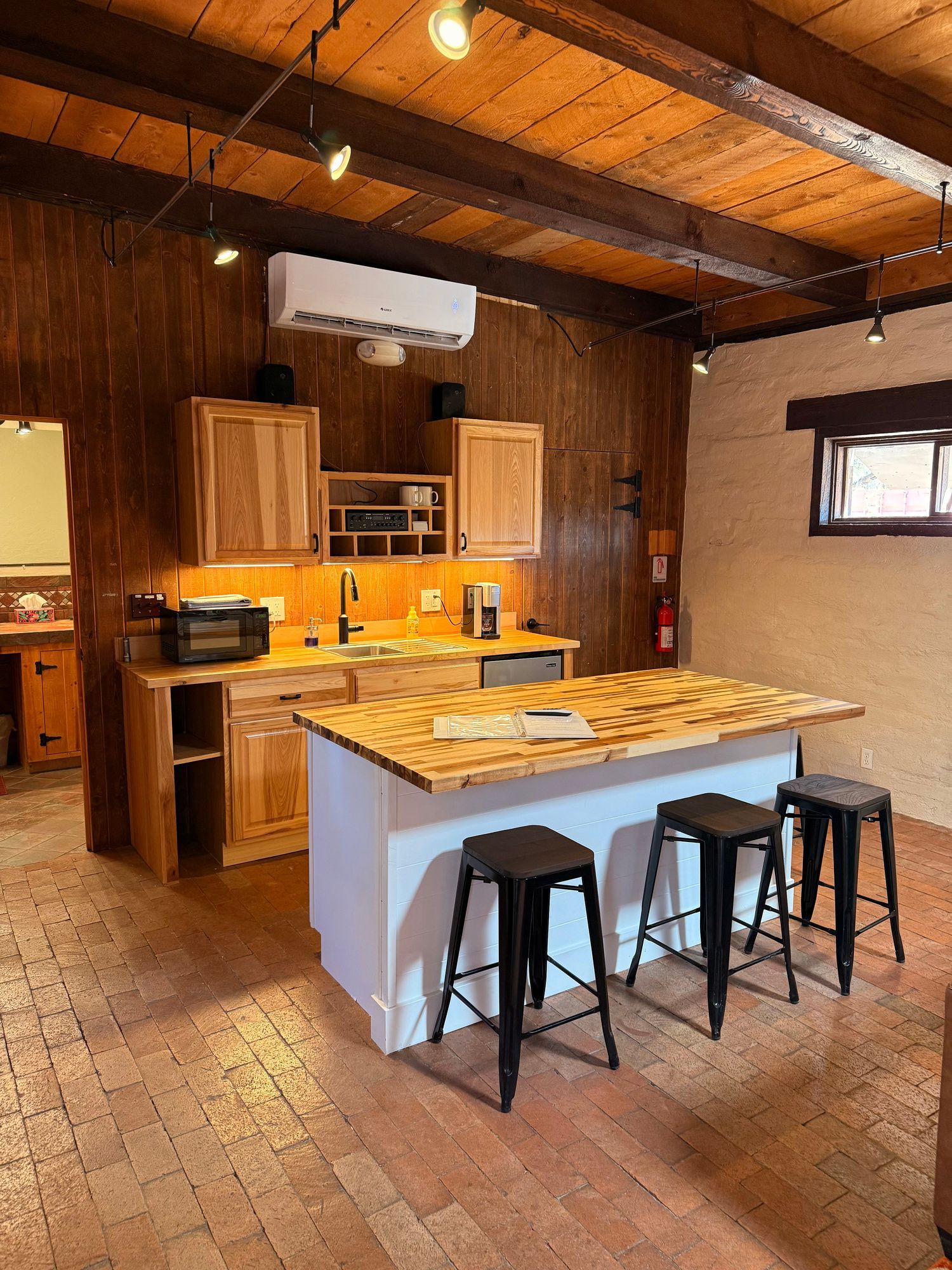 Cozy kitchen with wooden cabinets, white island, and black stools on a brick floor.