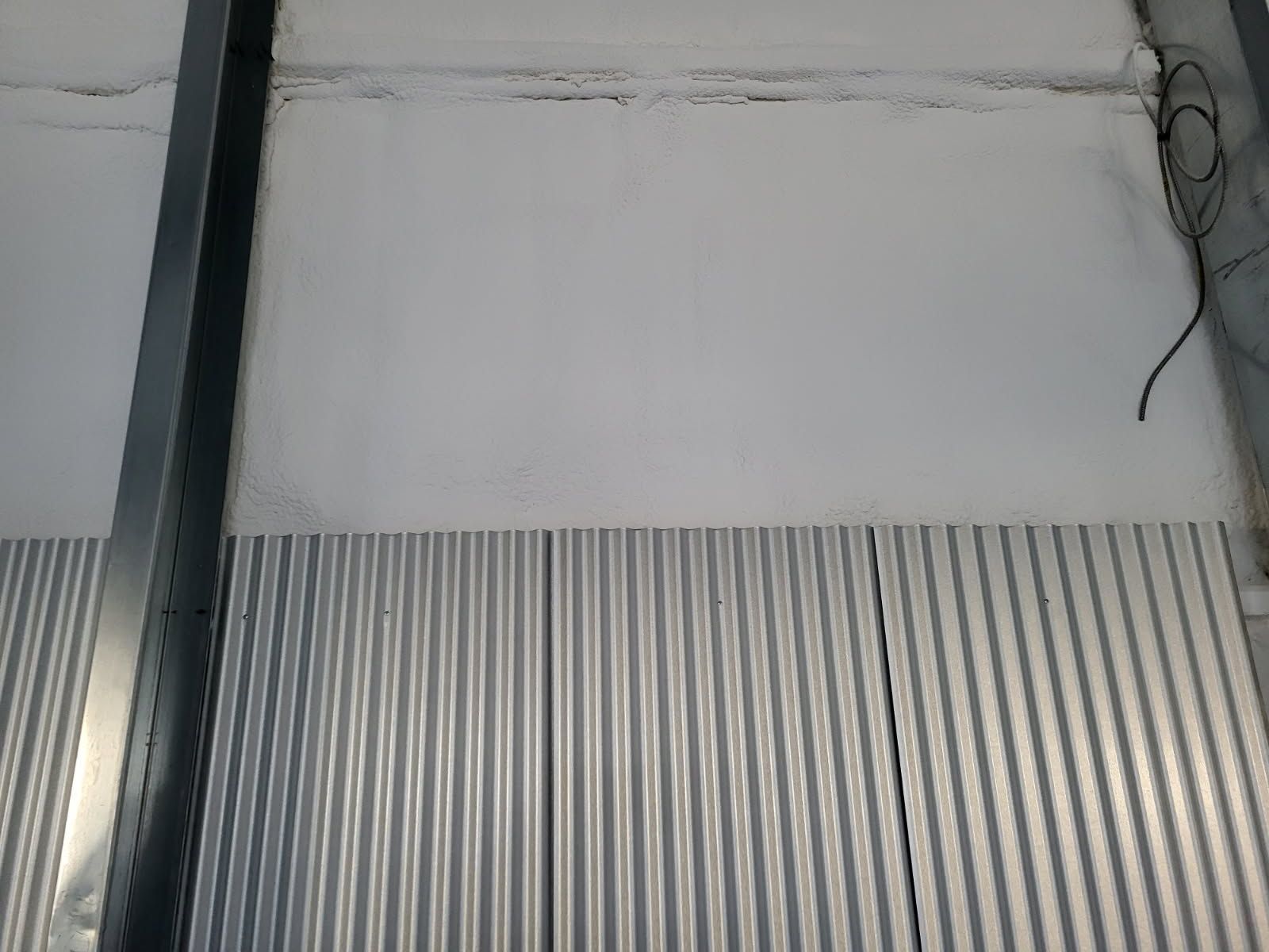 A close up of a metal wall with a white wall behind it.