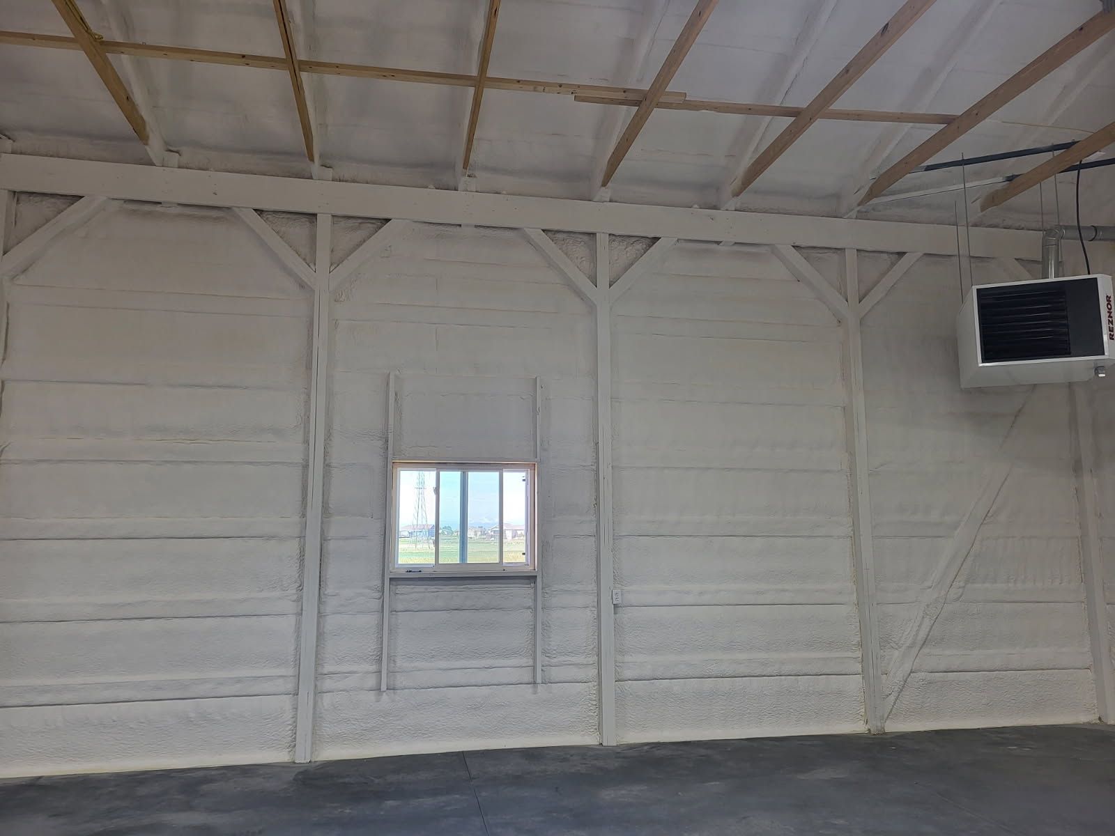 An empty room with a window and a heater hanging from the ceiling.