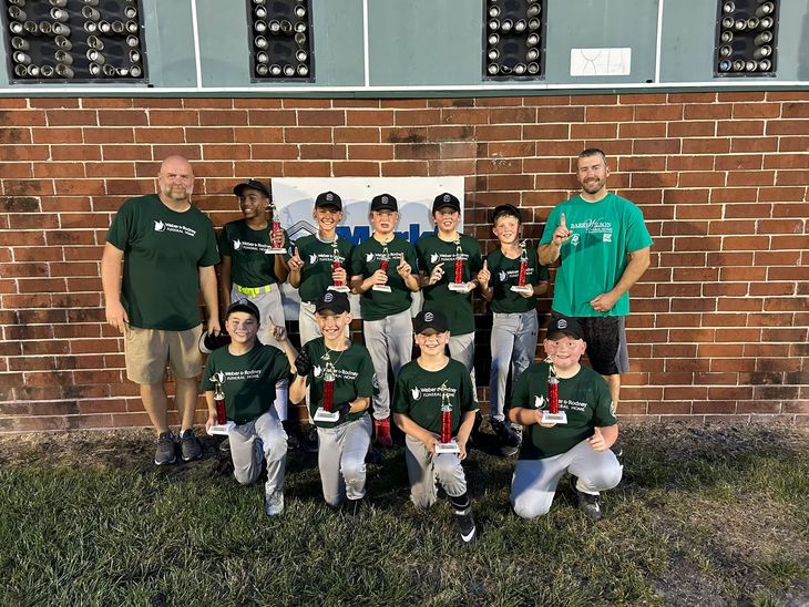 Youth baseball team and coaches posed in front of a brick wall at night.