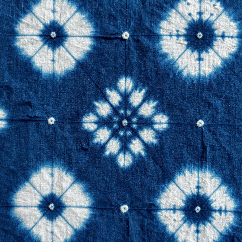 Indigo fabric with white tie-dye patterns. Square and floral designs on a grid.