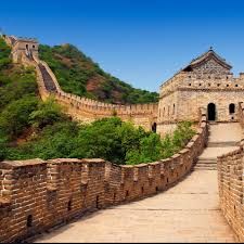 The Great Wall of China, a stone structure ascending a green, hilly landscape under a blue sky.