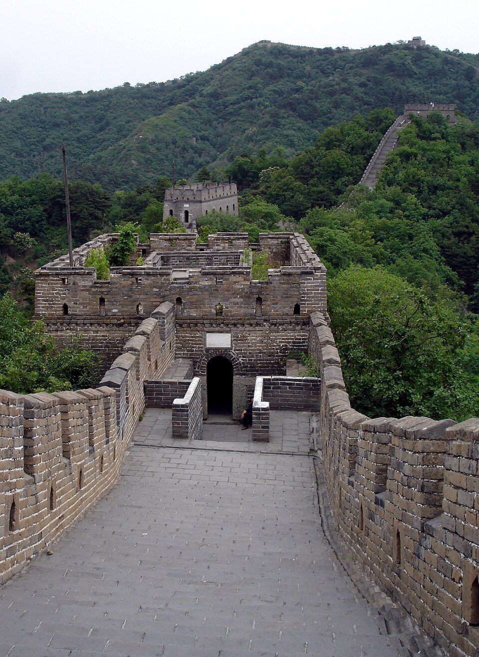 Stone walkway through a fortress gate on the Great Wall, with green hills in the background
