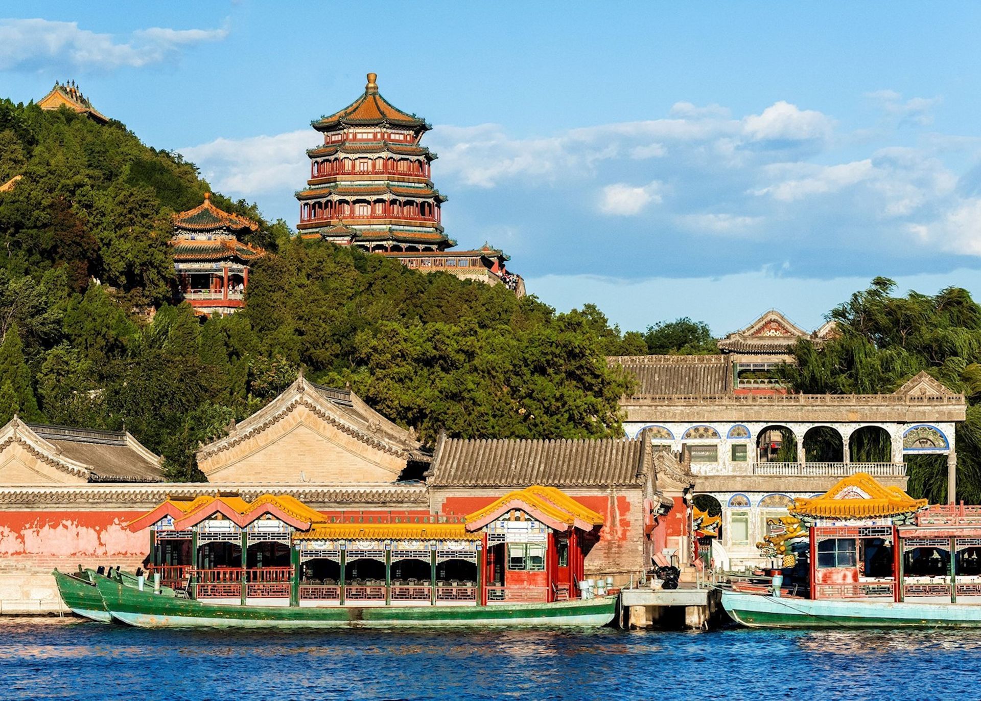 Boats on lake in front of Chinese temple buildings on a green hillside with a pagoda.