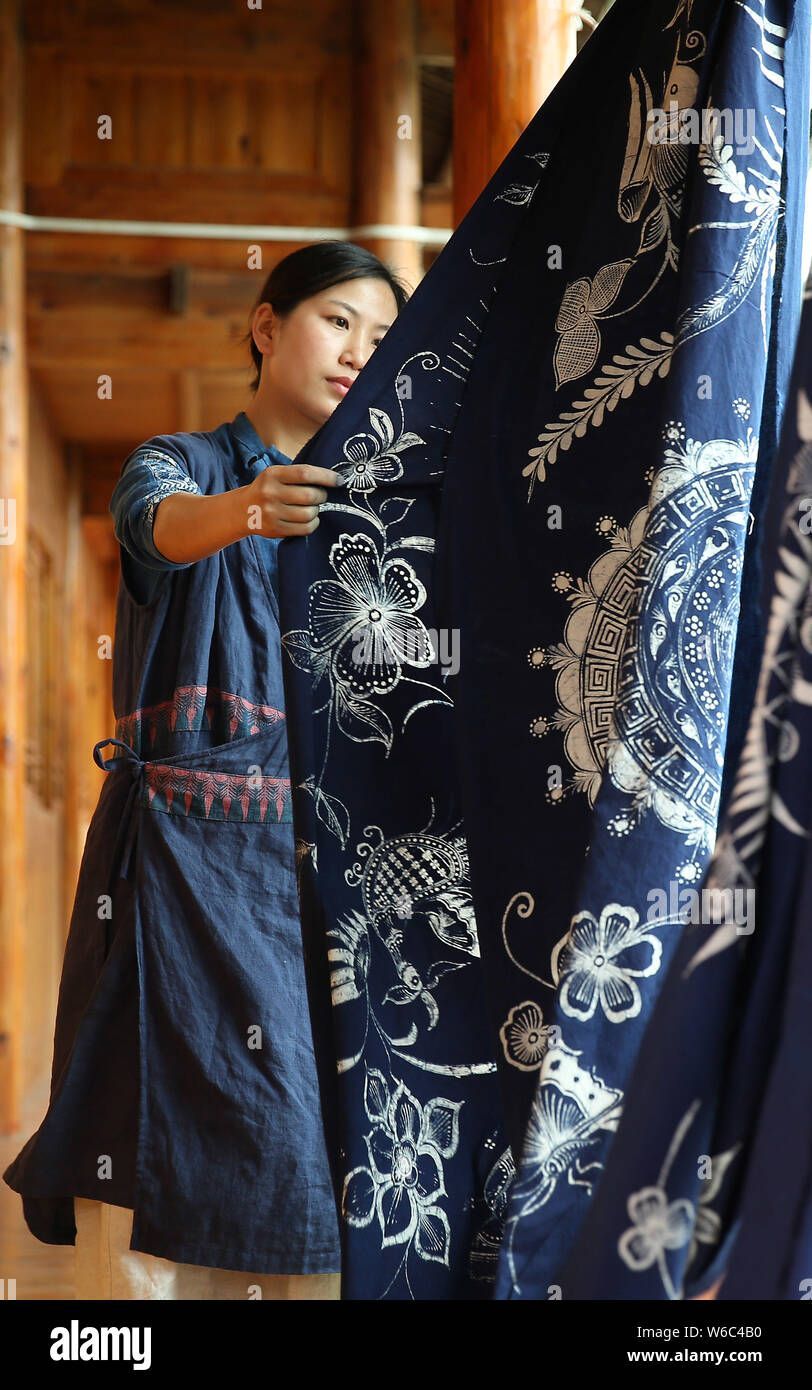 Woman holding up blue patterned fabric in a wooden building.