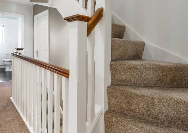 Staircase with beige carpet and white banister leading upstairs, hallway with a door.