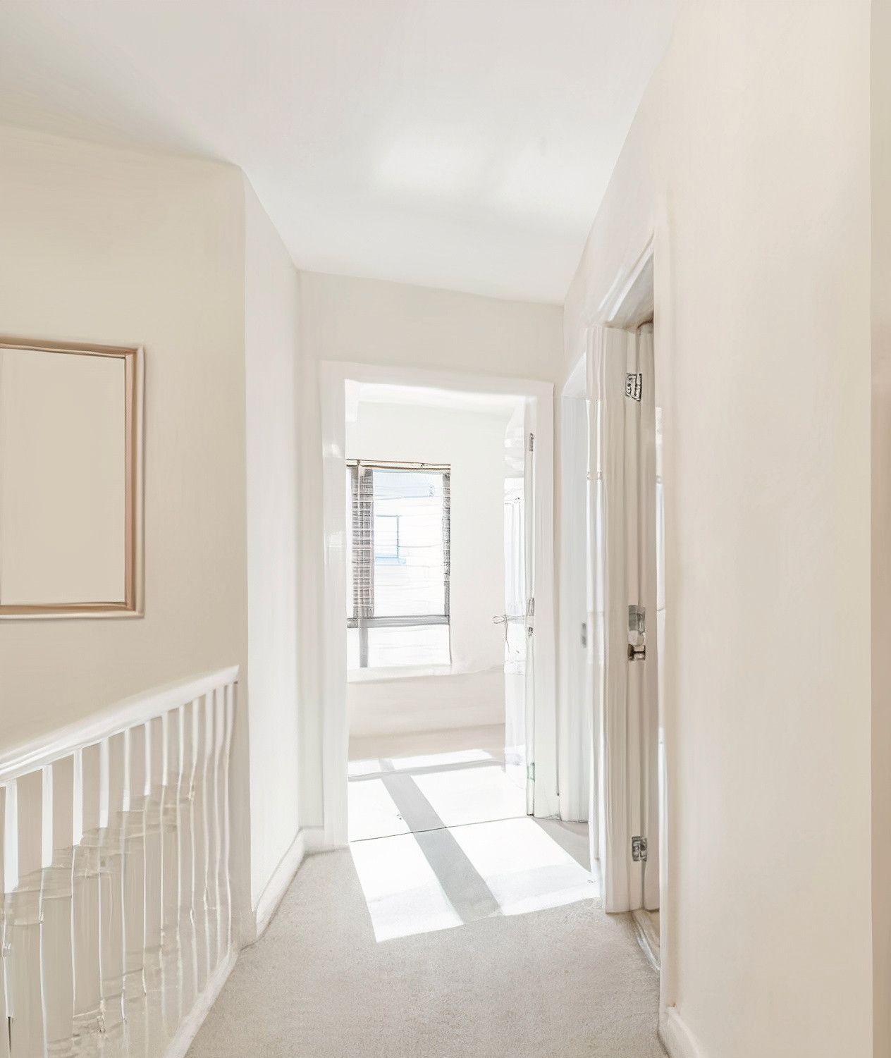 Hallway with light walls, carpet, and sunlight streaming from a window ahead.