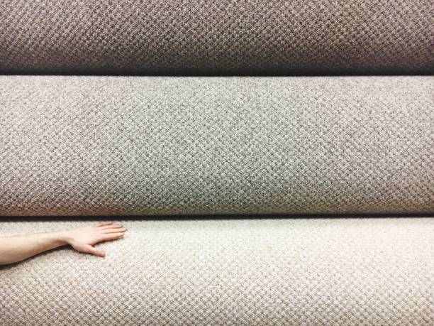 Hand next to beige carpet rolls in a store.