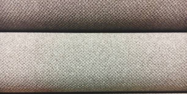 Hand touching a roll of beige carpet. Two more rolls stacked above.