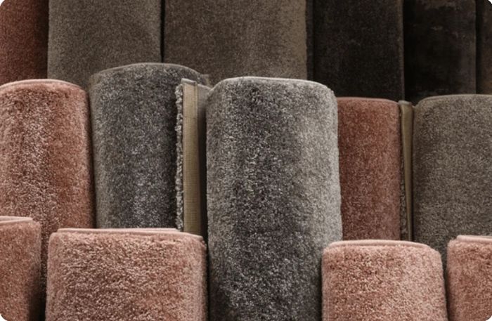 Rolled carpet samples in various shades of brown and gray, displayed for selection.