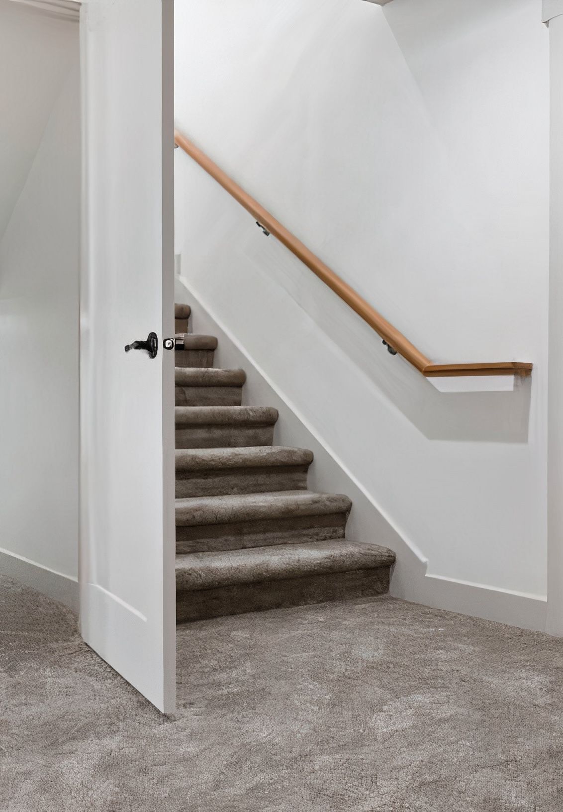 Door ajar, leading to carpeted stairs with wooden handrail against a white wall. The floor is also carpeted.