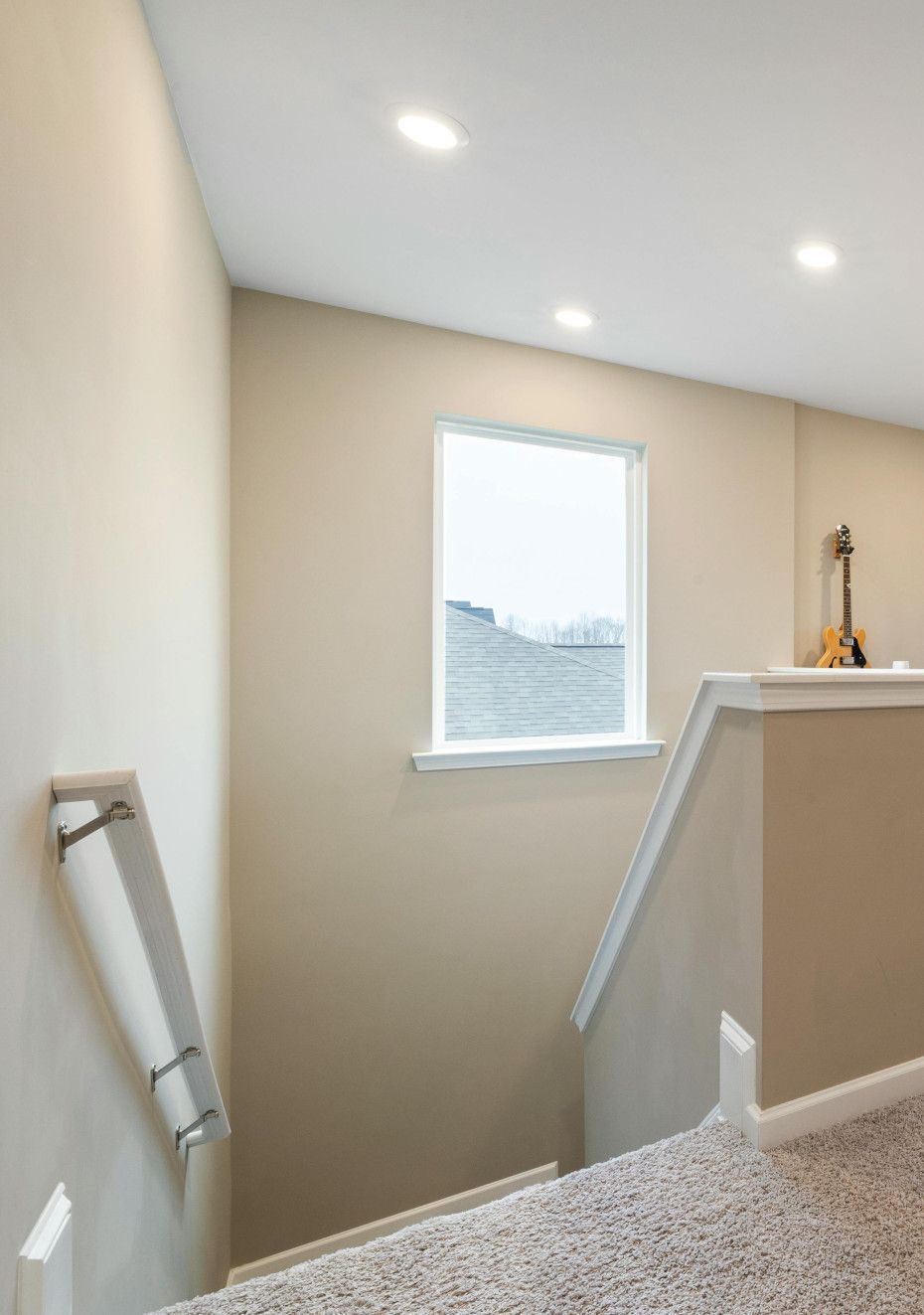 Stairway with beige walls and carpeted steps, a window, and recessed lighting. A handrail is mounted on the wall to the left.