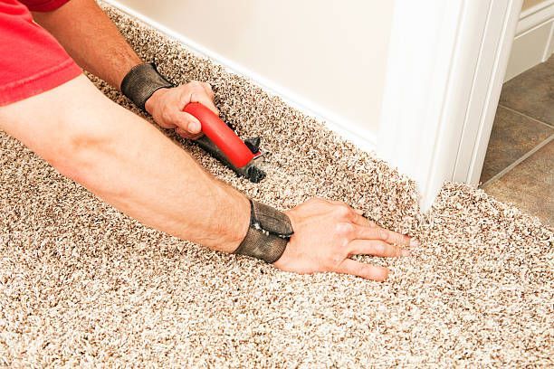 Person installing carpet near a wall; using a tool.