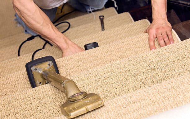 Person installing beige carpet on stairs with tools.
