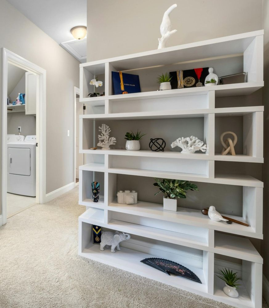 White, angular shelving unit in hallway displays decor items; doorway to laundry room on left.