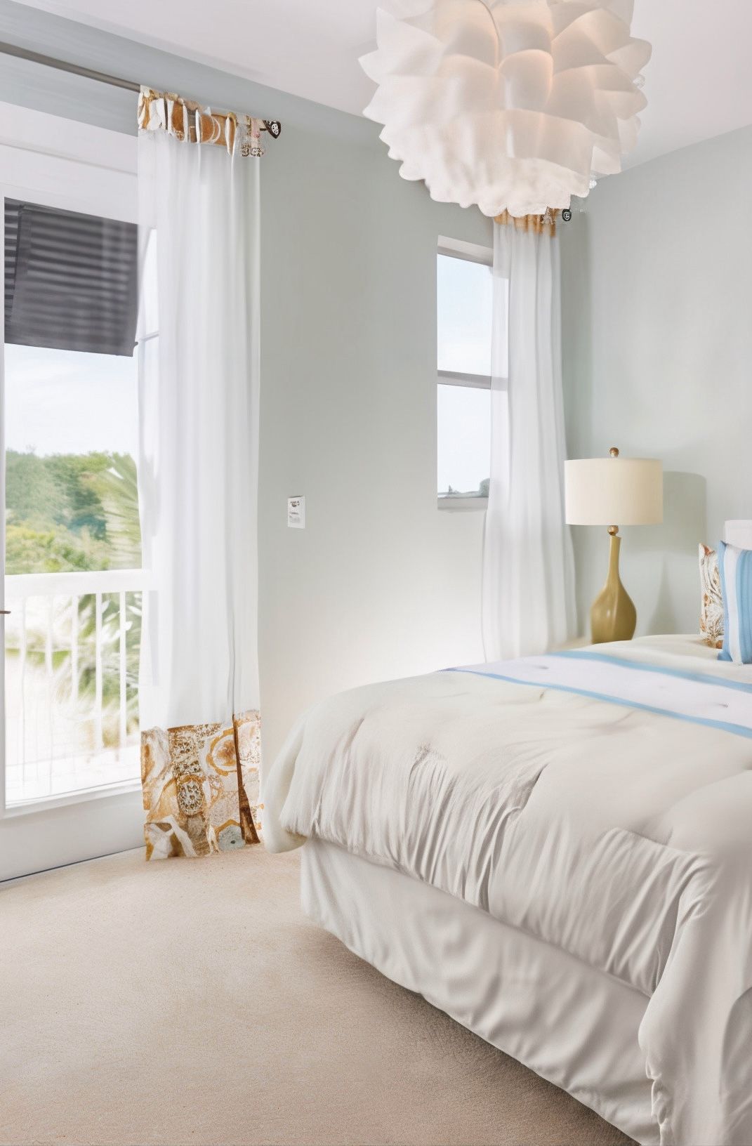 Bedroom with light blue walls, white bedding, sheer white curtains, and a large, white, flower-shaped light fixture.